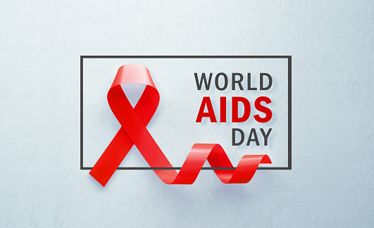 Red AIDS awareness ribbon sitting next to World AIDS Day message on grey background. Horizontal composition with copy space. World AIDS Day concept.