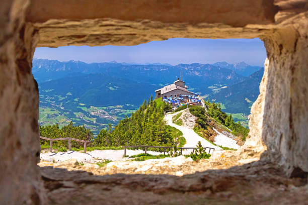 гнездо орла или укрытие kehlsteinhaus на скале над альпийским пейзажем панорамный вид через каменное окно - konigsee стоковые фото и изображения