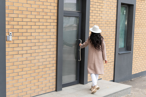 woman enters the building, holding the door handle, back view