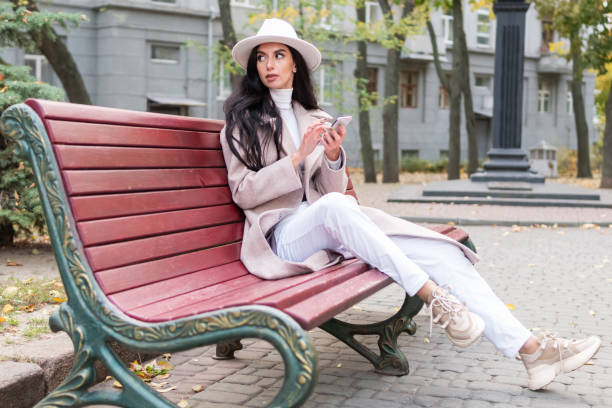 Beautiful woman sits on a bench in the city and writes a message on the phone