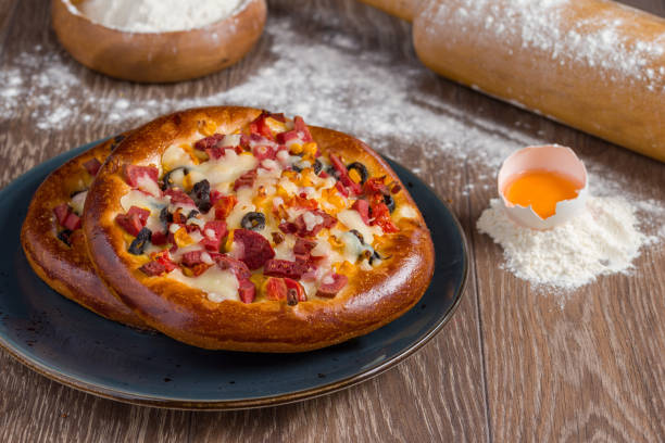 Small mixed pizza with pepperoni, sausage and cheese on wooden table.