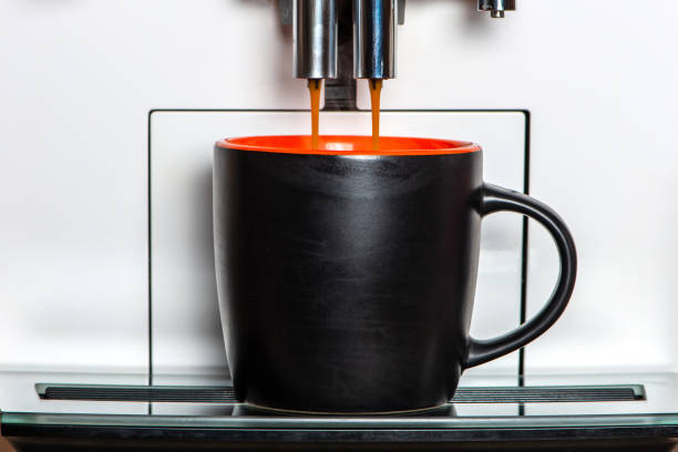 Coffee going out from a coffee machine in black mug. Front view, close up.