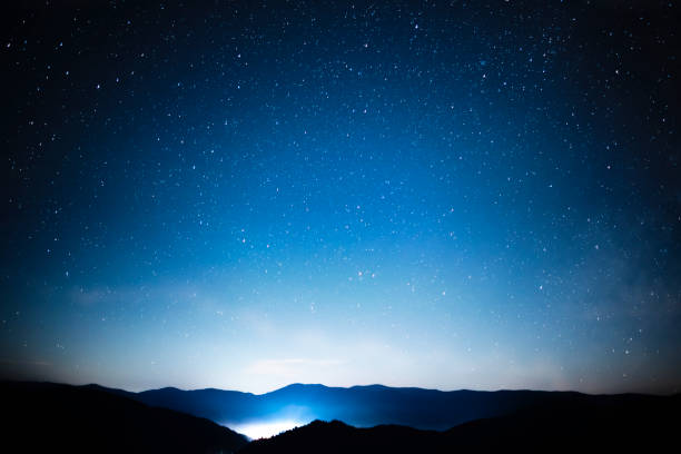 istock Starry night sky over mountains panorama with city lights below 1287299150