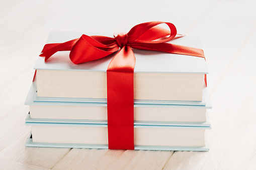 Books tied with gift ribbon on white wooden background: concept of donating books.