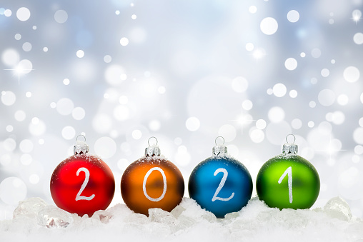 Multicolor baubles arranged in the year 2021, lying on ice, nice christmas defocus lights background.