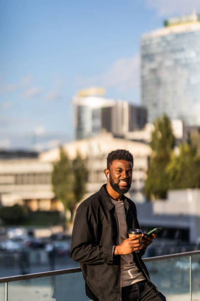 istock Young Smiling African man using smartphone on hands while standing at sunny city street. 1287304357