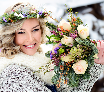 A beautiful woman with white teeth and a perfect smile holds a bouquet of roses and fir branches. Happy sincere winter outdoor portrait.