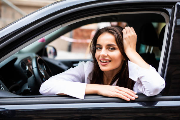 istock Happy young woman in sunglasses leaning on a window and looking away while sitting inside a car 1287314734