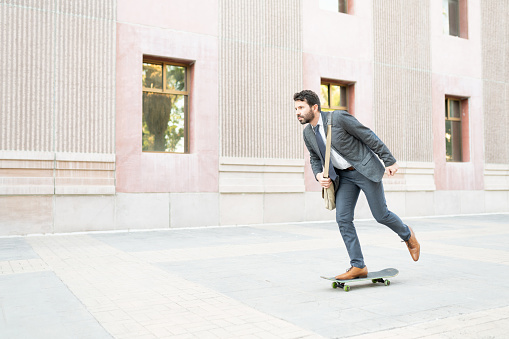 Businessman in his 30s with a suit skating to his work building. Latin man using an alternative transport to commute to his work