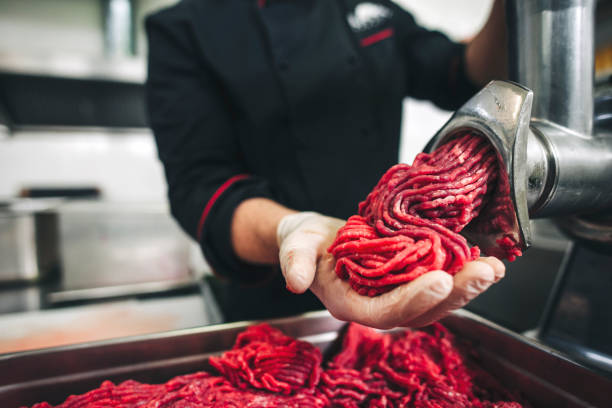 Male chef butcher doing fresh ground beef on the meat grinder Male chef  butcher doing fresh ground beef for burgers in the restaurant. He put small pieces of fresh beef meat in the grinder to make ground beef grinder stock pictures, royalty-free photos & images