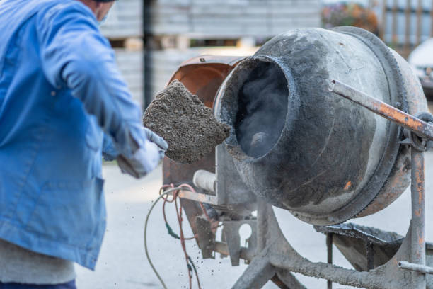 Unknown man using shovel to make cement concrete mortar mixture in mixer at construction site back view selective focus on mixer
