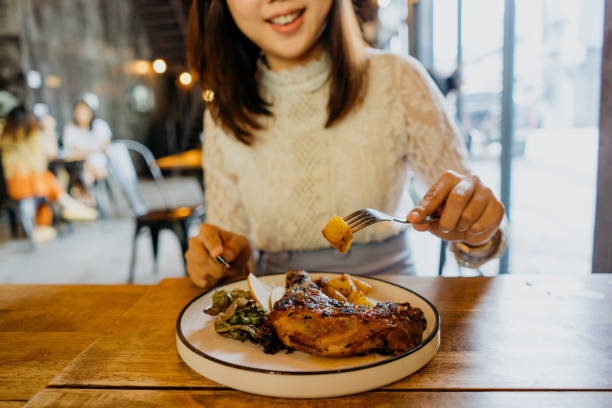 young asian woman enjoying a whole chicken leg meal in a cafe - asia cooked food gourmet imagens e fotografias de stock