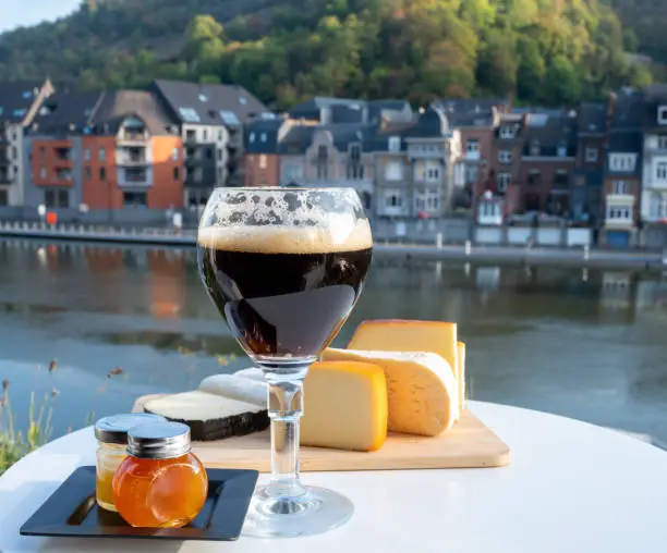 Drinking of dark and strong Belgian abbey beer with cheeses in sunny day with nice view on Maas river and town Dinant, Belgium