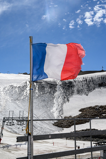 Blue-white-red national french flag waving on mast in French Alpine mountains with view on glacier in sunny day