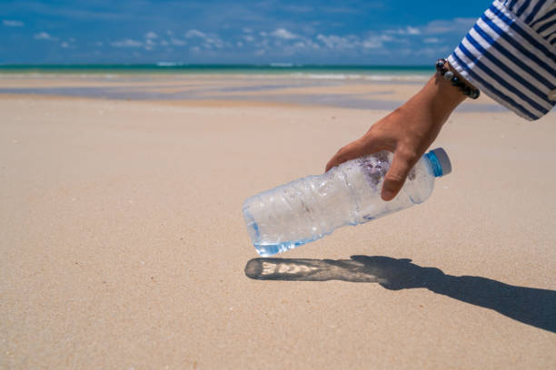 istock Hand pick up empty water bottle or trash at beautiful beach. Environment Global warming issue. 1287342570