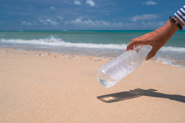 istock Hand pick up empty water bottle or trash at beautiful beach. Environment Global warming issue. 1287342632