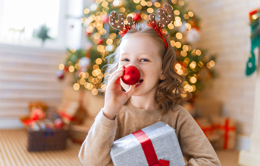 Merry Christmas and Happy Holidays! Cheerful cute child girl with gift. Kid is having fun near tree.