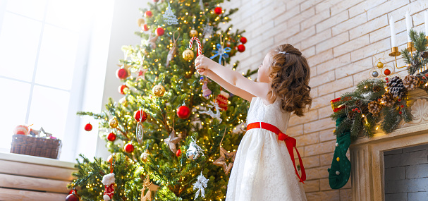 Merry Christmas and Happy Holidays! Cute little child girl is decorating the tree indoors. The morning before Xmas.