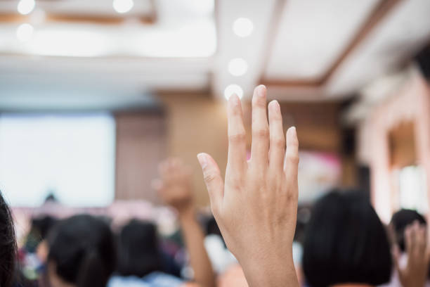 istock Audience or students raising hands up at conference to answer question while speaker speech at seminar hall with crowd groups, arms of large group in classroom for vote or questions 1287362993