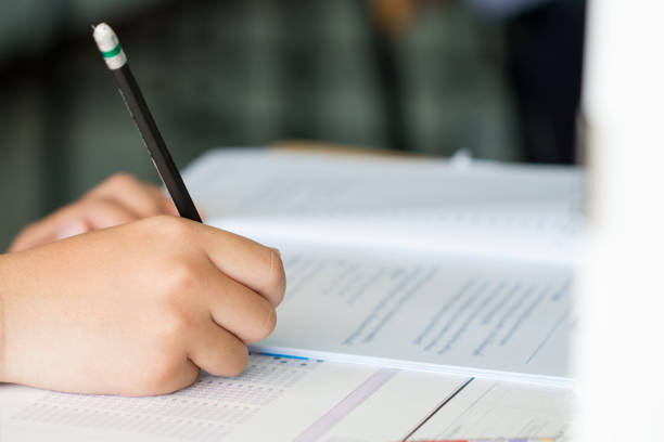 istock Exams test student in high school, university student holding pencil for testing exam writing answer sheet and exercise for taking in assessment paper on wood table classroom. Education study Concept 1287363586
