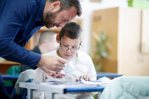 istock Special education teacher showing special needs boy how to fold paper 1287363993