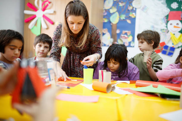 Special education teacher assisting elementary students in art class Special education teacher standing by the desk in art class and assisting elementary students special education stock pictures, royalty-free photos & images