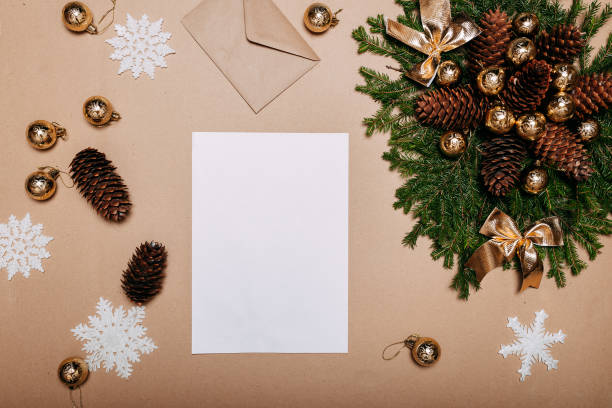 istock Christmas wreath decorations flat layout with space for text. Fir branches, pine cones, golden ornaments and craft envelope on the cardboard background. White sheet of paper in the center. 1287364198