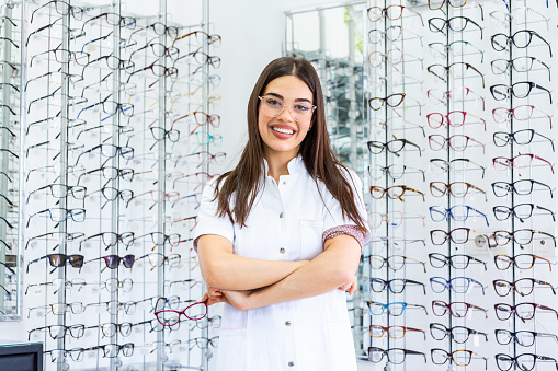 Optician selling glasses at the optics. Happy optician selling glasses and looking at the camera smiling. Friendly eye doctor selling glasses at an optician's shop and looking at the camera smiling