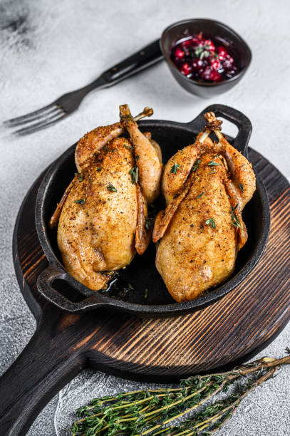 istock Whole roast quails in a pan.  White background. Top view 1287366394