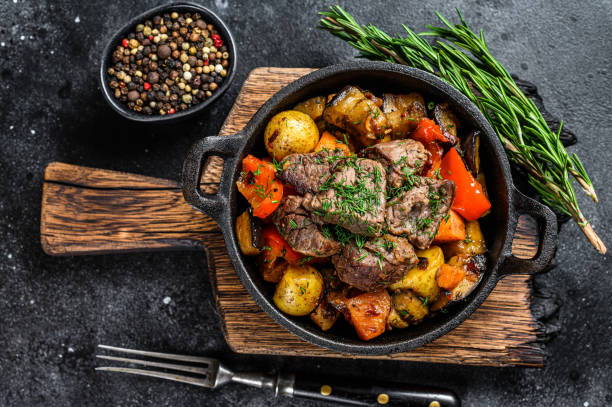 istock Meat stew in cooking pot on dark rustic cutting board. Black background. Top view 1287370259