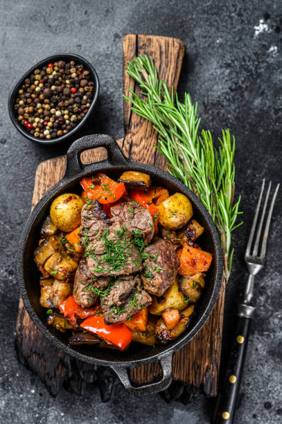 istock Meat stew in cooking pot on dark rustic cutting board. Black background. Top view 1287370272