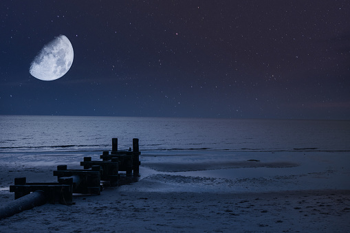 A Night Sky With a Half Moon and Stars Over the Beach and Ocean With a Pipe