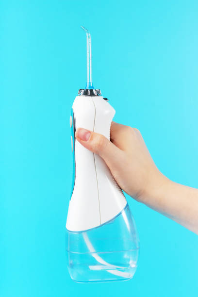 istock Woman's hand holds a dental irrigator on blue background. 1287371935