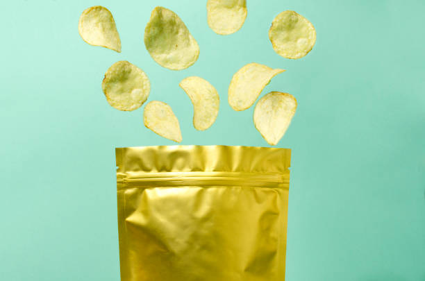 Falling potato chips into the golden package against blue background Vertical image.Closeup of tasty crispy potato chips as a background gold potato stock pictures, royalty-free photos & images