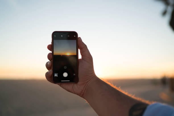 Cropped image of man's hand holding modern smartphone using application for taking evening photos of beautiful sundown, closeup view of male shooting video of sunset and skyline on telephone camera imagen recortada de la mano del hombre sosteniendo el teléfono inteligente moderno usando la aplicación para tomar fotos de la noche de la puesta del sol hermosa, vista de cerca del vídeo de disparo masculino de la puesta de sol y el horizonte en la cá