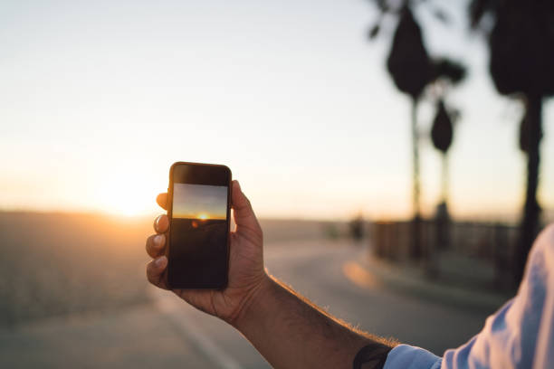 Close up view of male shooting video of sunset and skyline on smartphone camera, cropped image of man's hand holding mobile phone using app for making pictures of sundown during summer vacation vista de cerca de vídeo de disparo masculino de la puesta de sol y el horizonte en la cámara del teléfono inteligente, imagen recortada de la mano del hombre sosteniendo el teléfono móvil usando la aplicación para hacer fotos de la puesta del sol dur