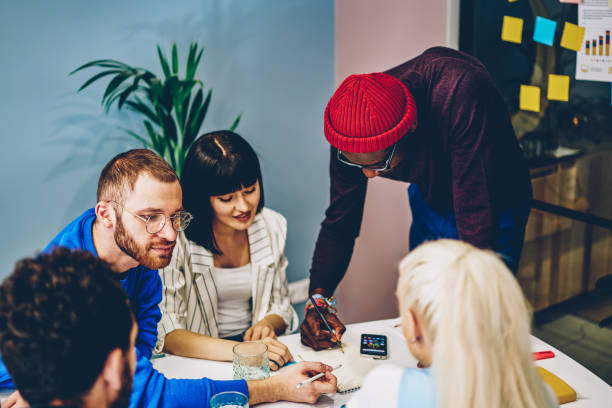 istock Diverse team of creative young people dressed in smart casual wear writing plan in notepad and collaborating on common design project at meeting table having brainstorming session in modern office 1287374543