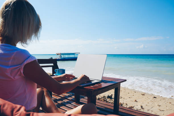 Back view of young millennial girl keyboarding publication for blog on netbook using good wireless internet connection on ocean beach,business woman enjoying freelance job using laptop near sea vista posterior de la joven chica milenaria publicación de teclado para blog en netbook utilizando una buena conexión inalámbrica a internet en la playa del océano, mujer de negocios disfrutando de un trabajo independiente usando portátil cerca del ma