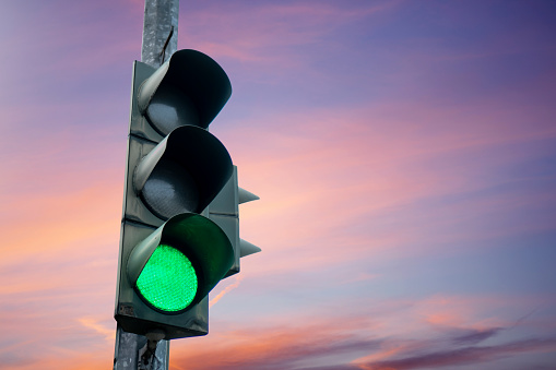 Traffic light in green color, with the dusk sky in the background.