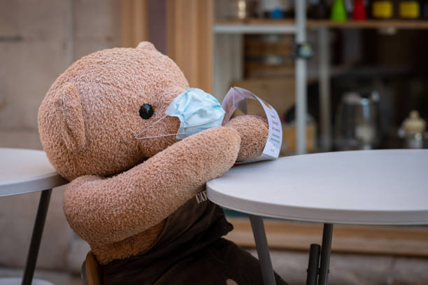 istock Big stuffed bear with face mask sitting on a table 1287376216