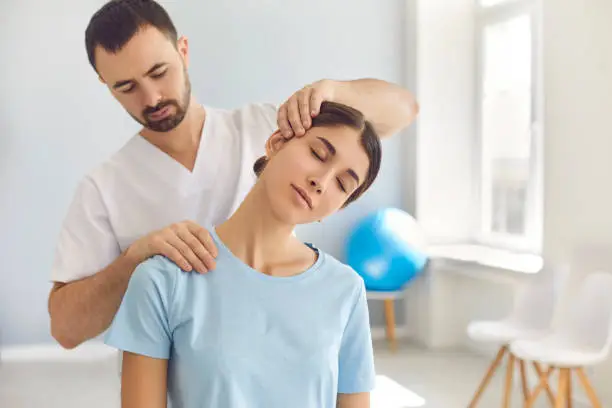 Photo of Licensed chiropractor doing neck adjustment to female patient in modern medical office