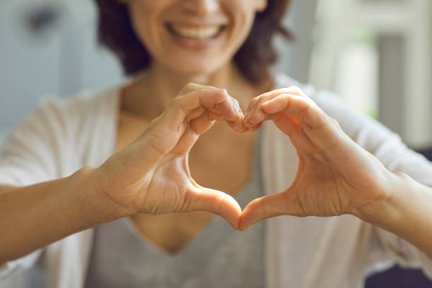 Cropped shallow focus image of happy smiling lady showing heart symbol with her hands Soft focus close up of happy smiling lady showing heart symbol with hands. Caring woman doing heart shaped gesture advertising health insurance, promoting charity effort, expressing love and gratitude heart health stock pictures, royalty-free photos & images
