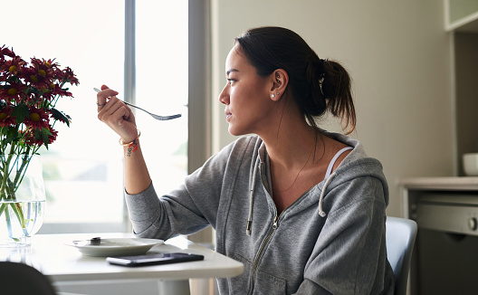 Cropped shot of a woman eating breakfast while sitting at home