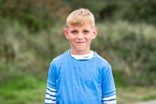 A portrait shot of a young caucasian boy in a rural outdoor setting looking at the camera with a positive emotion and wearing casual clothing.