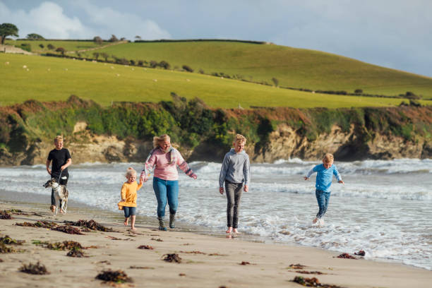 Family Adventures at the Beach A single mother and her four children walking along a beach on a day in autumn. One of the boys is walking their dog while another runs through the sea and they are all wearing casual clothing. They are on a staycation to lower their carbon footprint and support the local economy. 12 13 years pre adolescent child female blond hair stock pictures, royalty-free photos & images