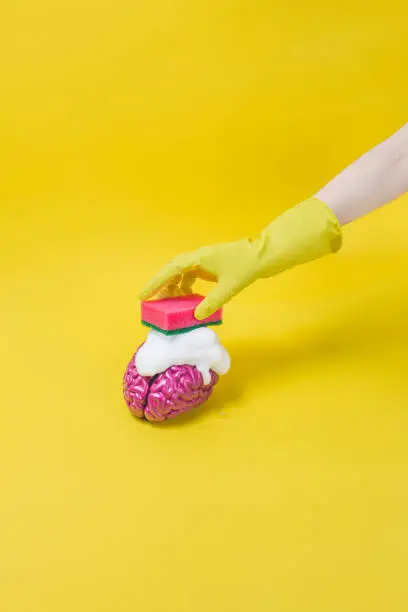 Funny concept image on brainwashed topic. Hand scrubbing a rubber brain on yellow background.