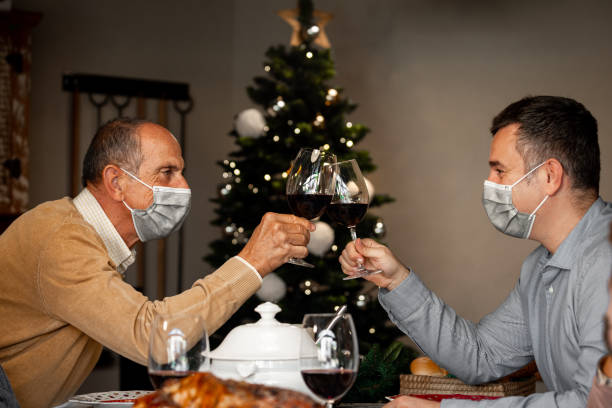 Grandfather and son in surgical masks toast during Christmas. Close up of grandfather and son in surgical masks toast at the Christmas Thanksgiving table at home in the year of the Coronavirus. New rules, Covid outbreak, coronavirus pandemic, lockdown. thanksgiving holiday covid stock pictures, royalty-free photos & images