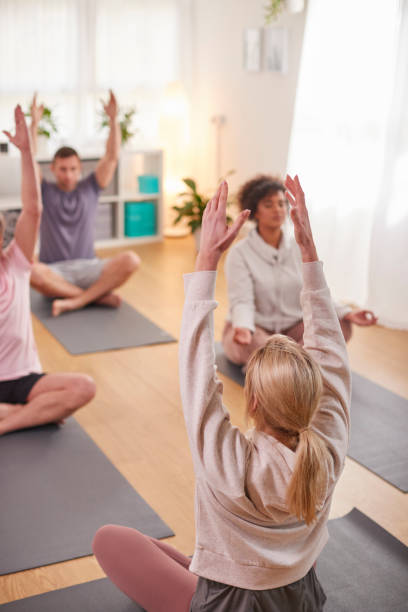 istock Group With Teacher Sitting On Exercise Mats Stretching In Yoga Class Inside Community Center 1287394809
