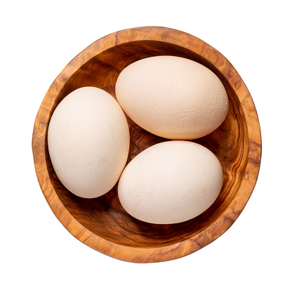 Raw chicken eggs in wooden bowl isolated on white background. Top view.