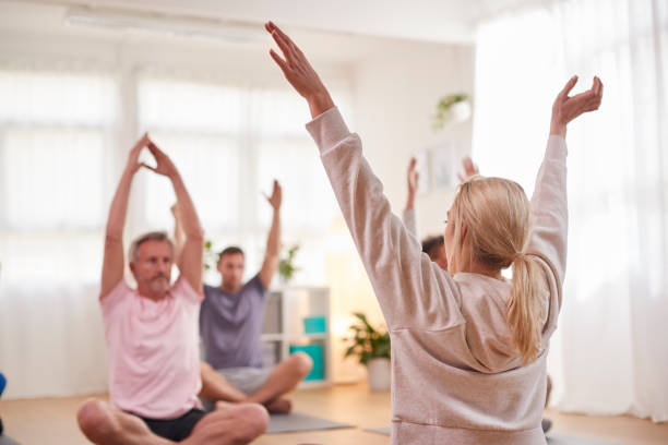 istock Group With Teacher Sitting On Exercise Mats Stretching In Yoga Class Inside Community Center 1287394879